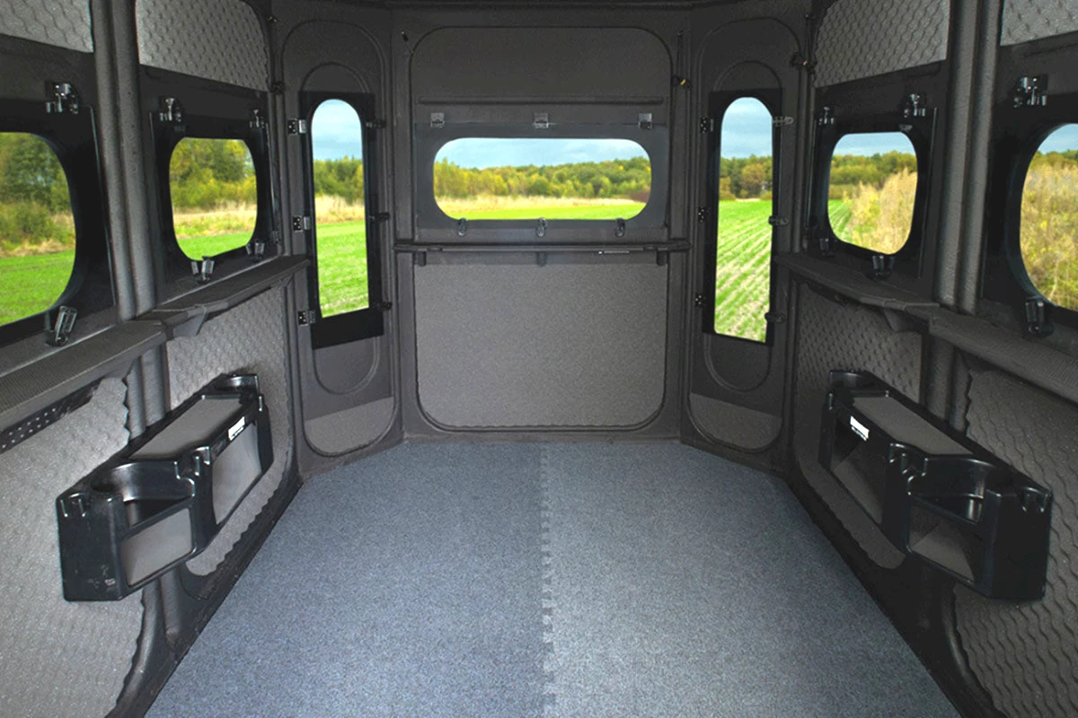 Interior of the 6'x8' Game Changer Platinum 360 looking toward the front windows, showing two pre-installed gear consoles and the marine-carpeted floor.