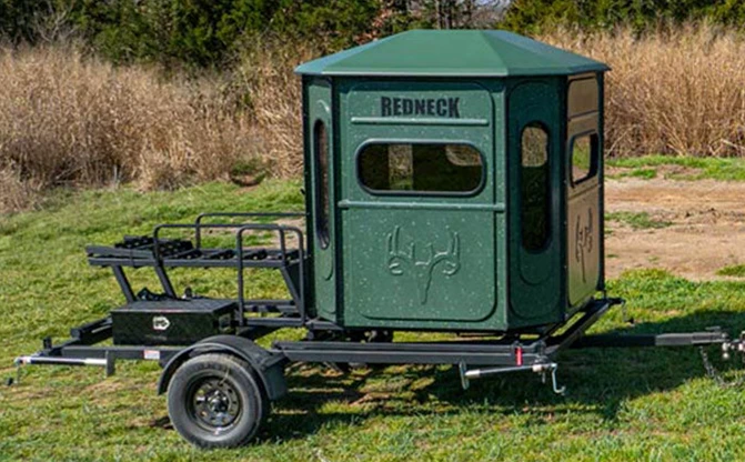 8 foot hydraulic blind trailer lowered in a field with a green Buck Palace blind mounted on top.