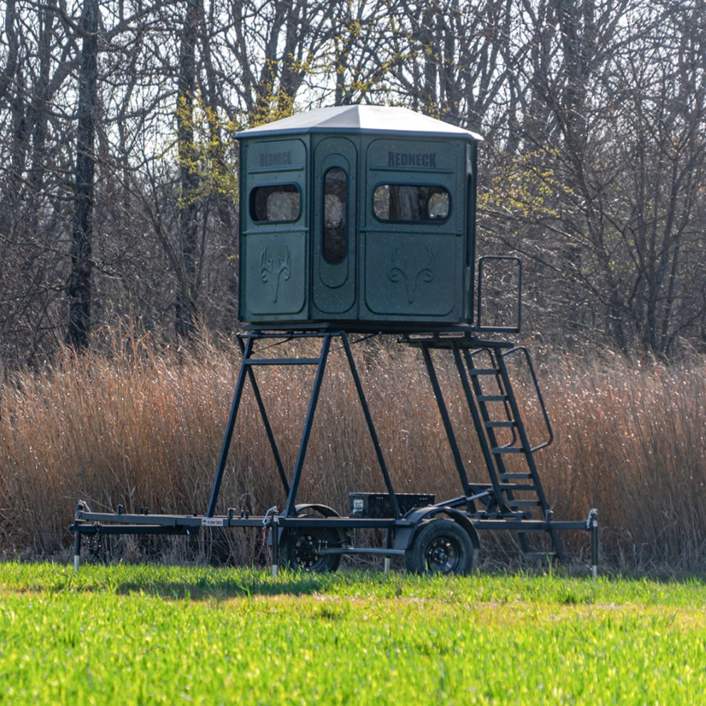 8 foot hydraulic blind trailer raised in a field with a box blind mounted on top.